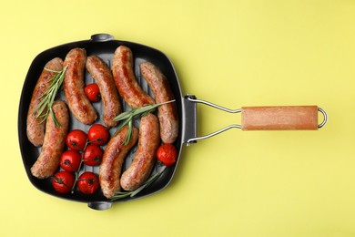 Photo of Grill pan with tasty homemade sausages, rosemary and tomatoes on yellow table, top view