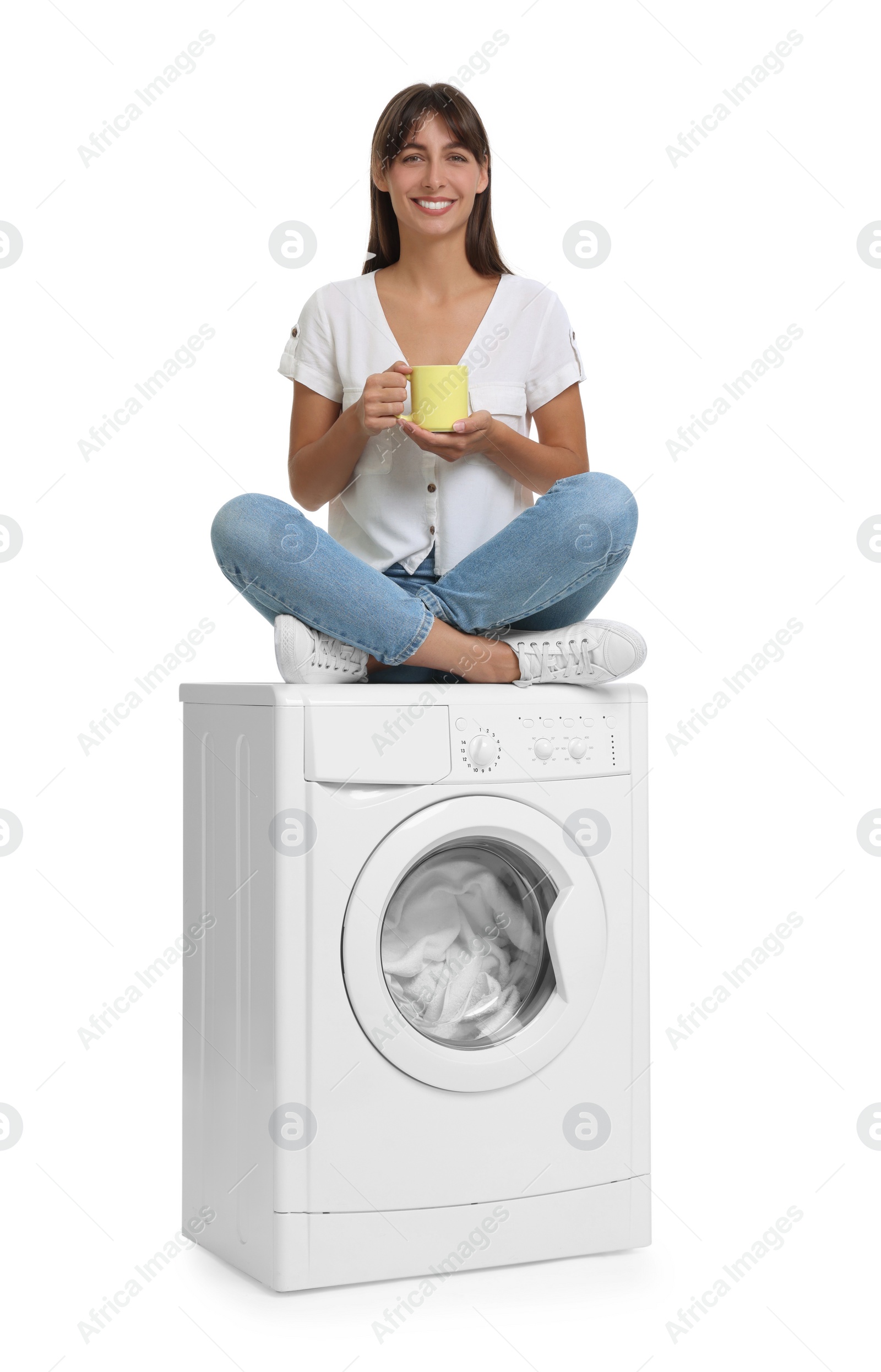 Photo of Beautiful woman with cup of drink sitting on washing machine against white background