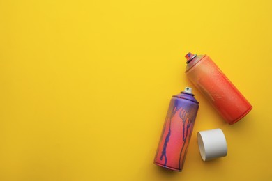 Photo of Used cans of spray paints on yellow background, flat lay with space for text. Graffiti supplies