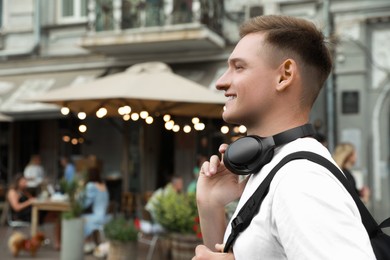 Photo of Smiling man with headphones walking outdoors. Space for text