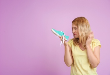 Photo of Young woman with stinky shoe on color background. Air freshener