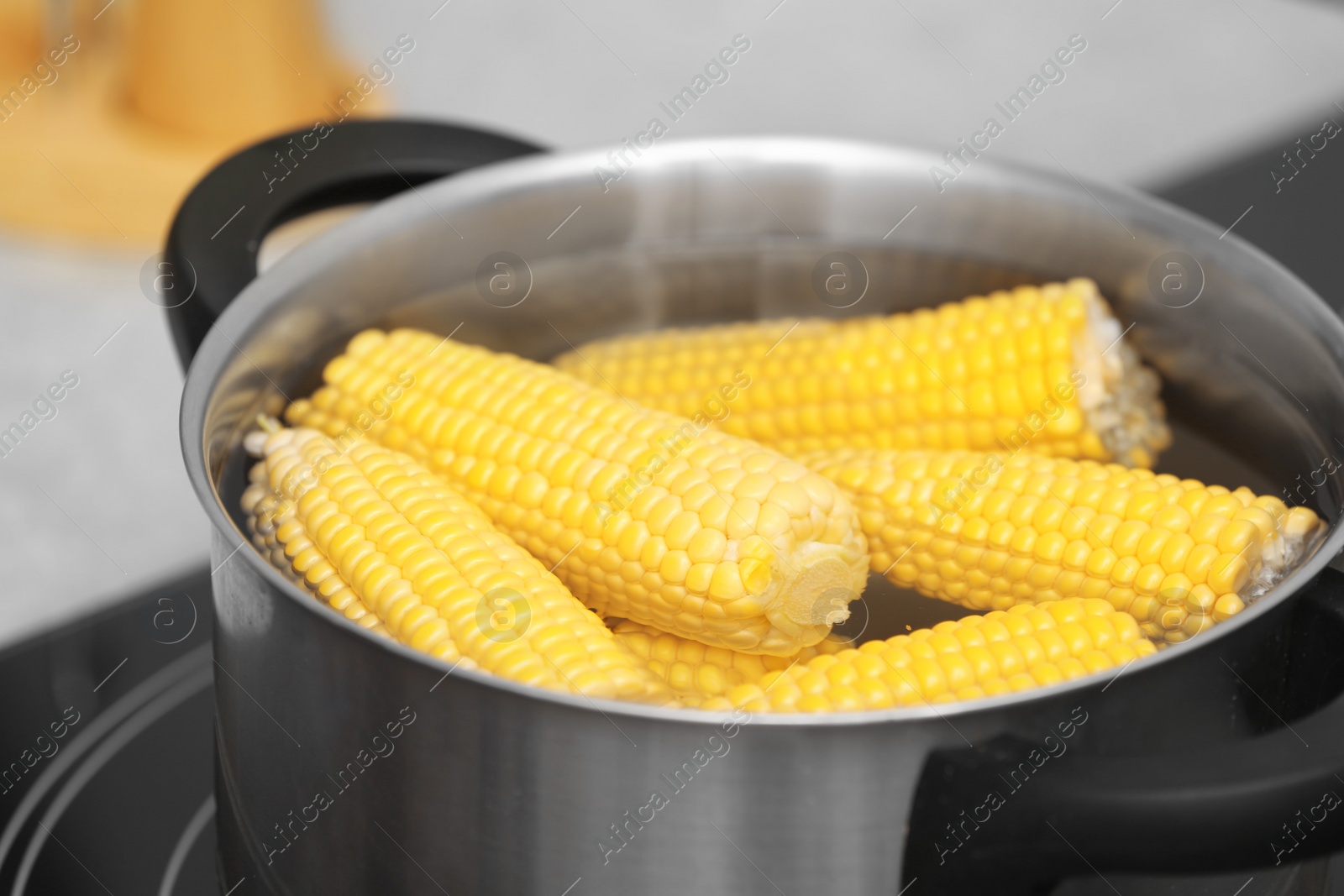 Photo of Stewpot with water and corn cobs on stove, closeup