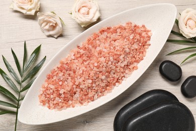 Photo of Natural sea salt, spa stones, palm leaves and roses on wooden table, flat lay