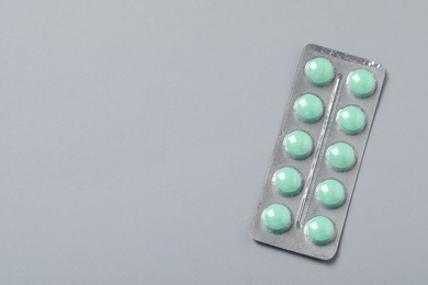Photo of Green pills in blister on grey background, top view. Space for text
