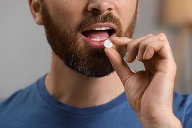 Closeup view of bearded man taking pill on blurred background