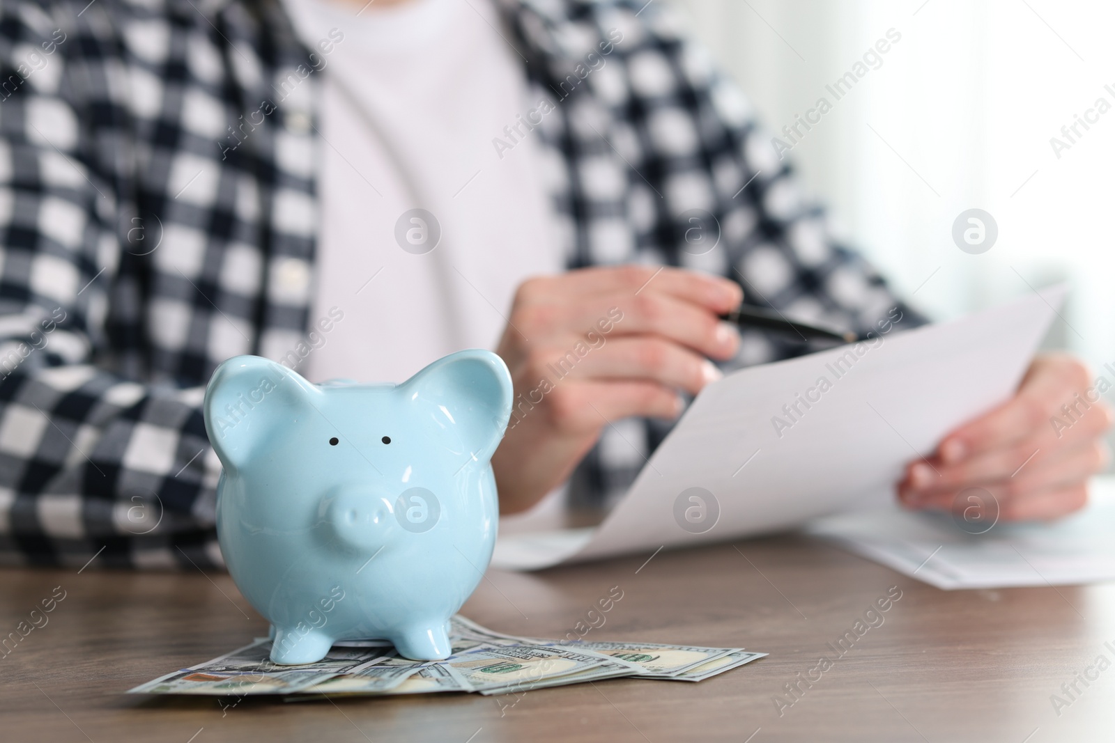 Photo of Financial savings. Man with document and pen at wooden table, focus on piggy bank