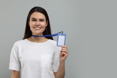 Photo of Happy woman holding vip pass badge on grey background, space for text