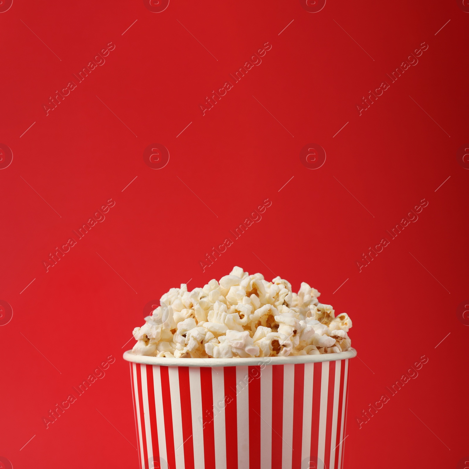 Photo of Delicious popcorn in paper cup on red background, closeup