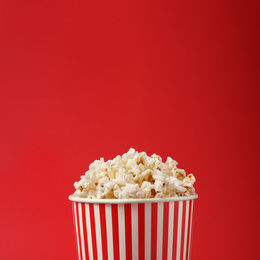 Photo of Delicious popcorn in paper cup on red background, closeup