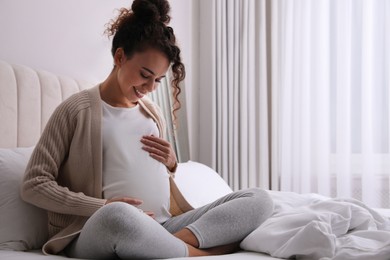 Photo of Pregnant young African-American woman sitting on bed at home