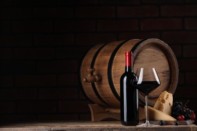 Photo of Delicious wine, cheese, grapes and wooden barrel on table against black background. Space for text