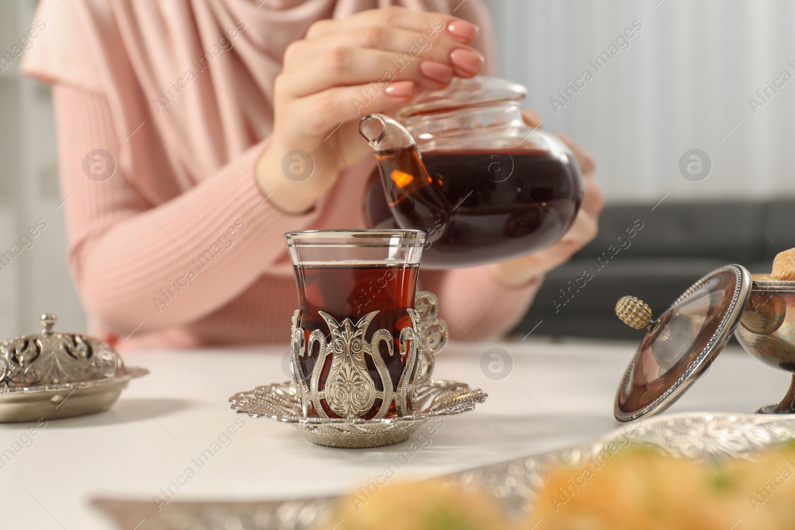 Photo of Woman pouring delicious Turkish tea from teapot into cup at white table, closeup