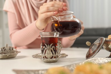 Photo of Woman pouring delicious Turkish tea from teapot into cup at white table, closeup