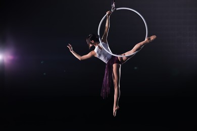 Photo of Young woman performing acrobatic element on aerial ring against dark background