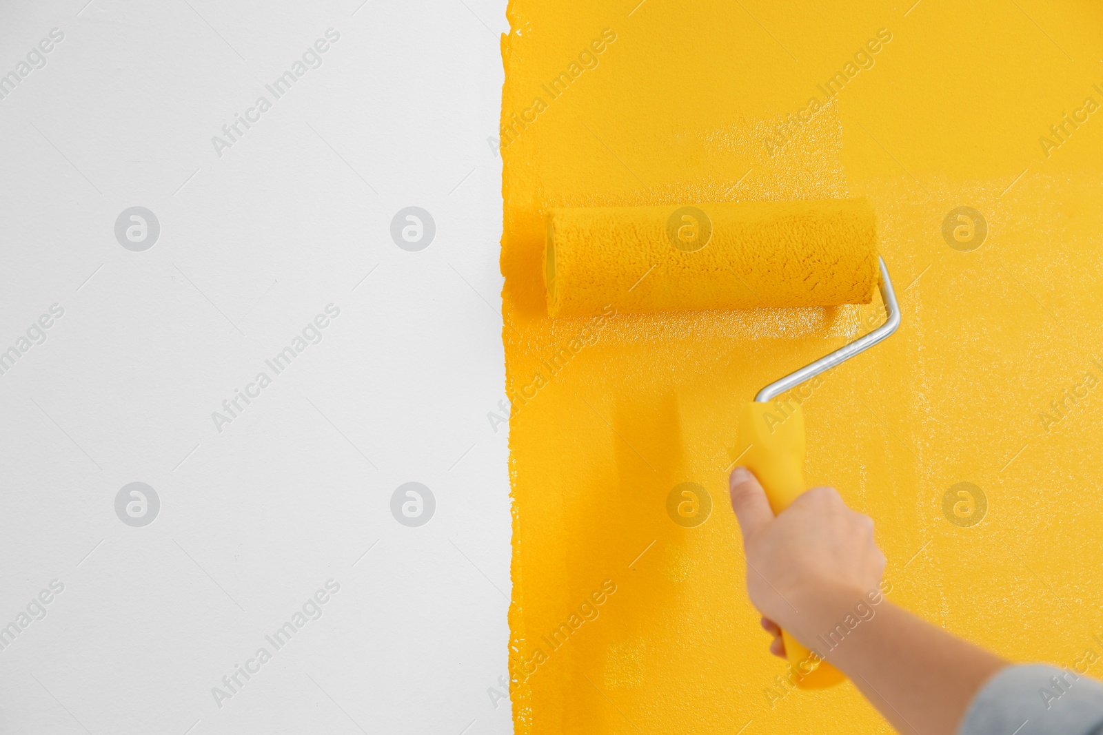 Photo of Woman painting white wall with yellow dye, closeup. Interior renovation