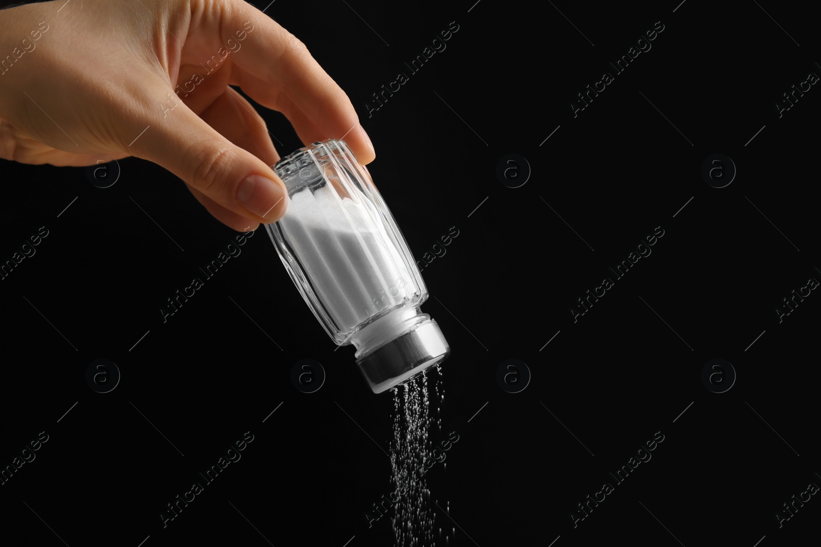 Photo of Woman pouring salt from shaker on black background, closeup