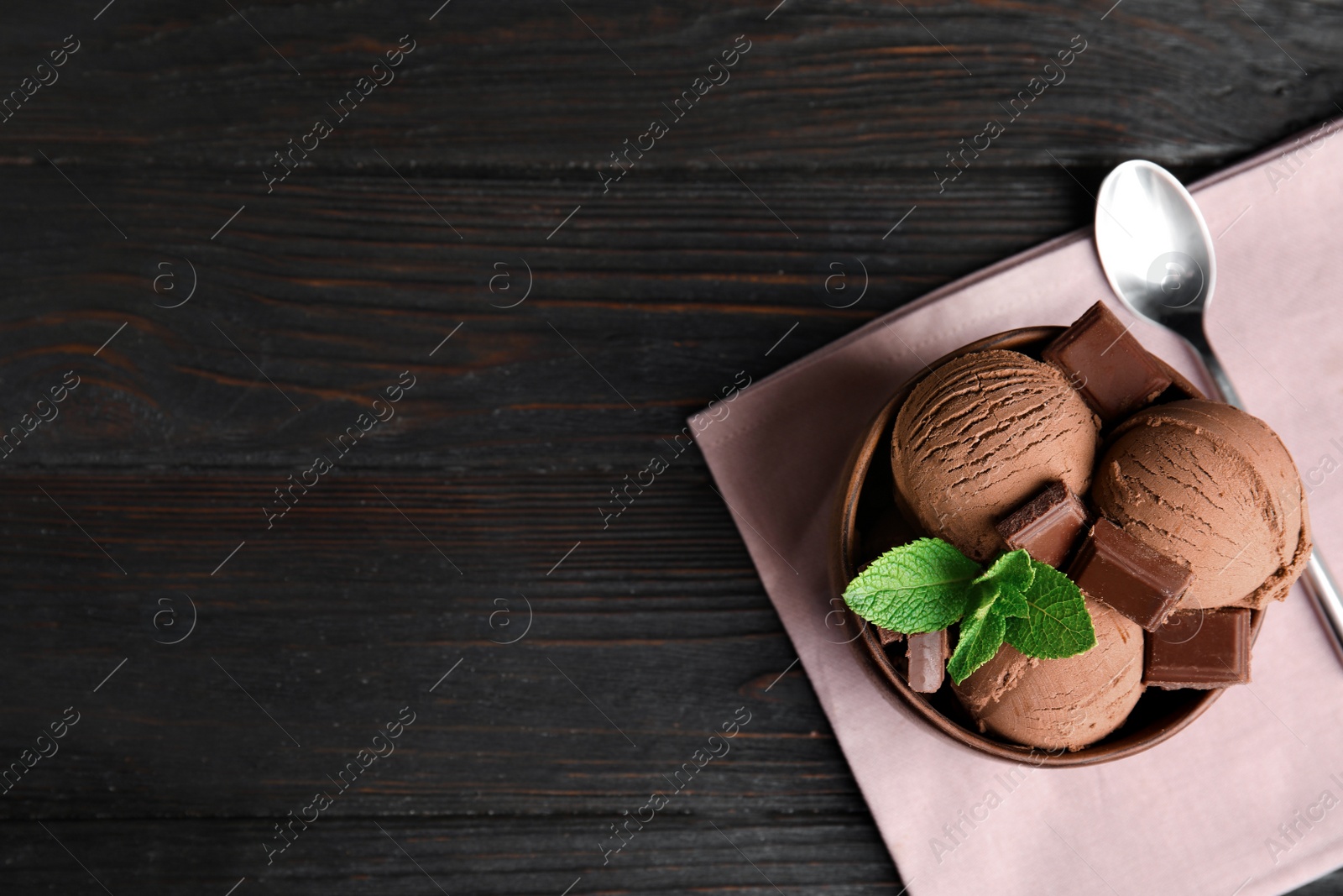 Photo of Wooden bowl of chocolate ice cream served on dark table, flat lay with space for text