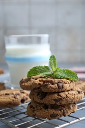 Photo of Tasty chocolate chip cookies, glass of milk and mint leaves on light grey table, closeup
