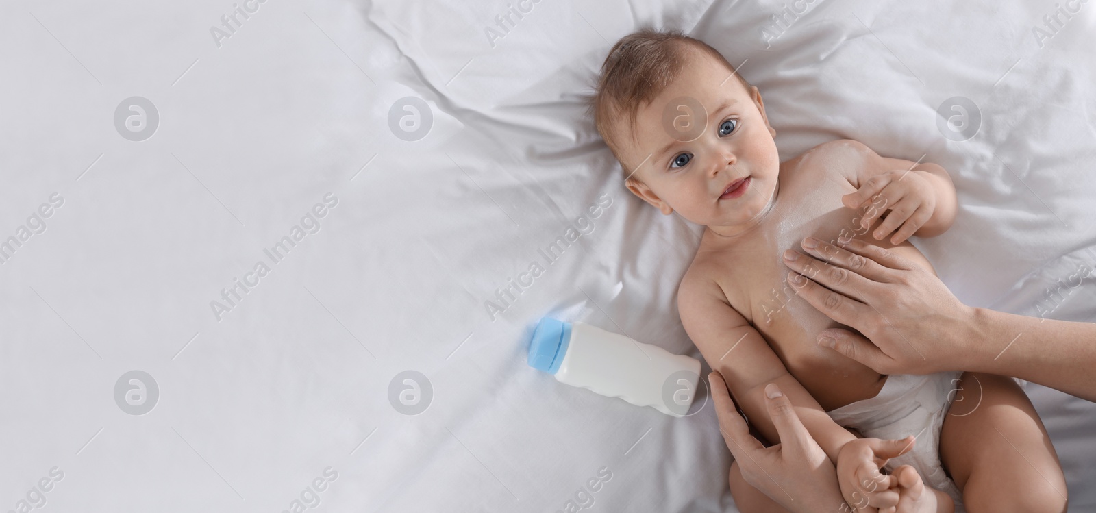 Image of Mother applying dusting powder onto her baby on bed, top view with space for text. Banner design