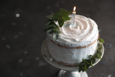 Photo of Tasty Birthday cake with burning candle and eucalyptus branches on grey table, closeup. Space for text