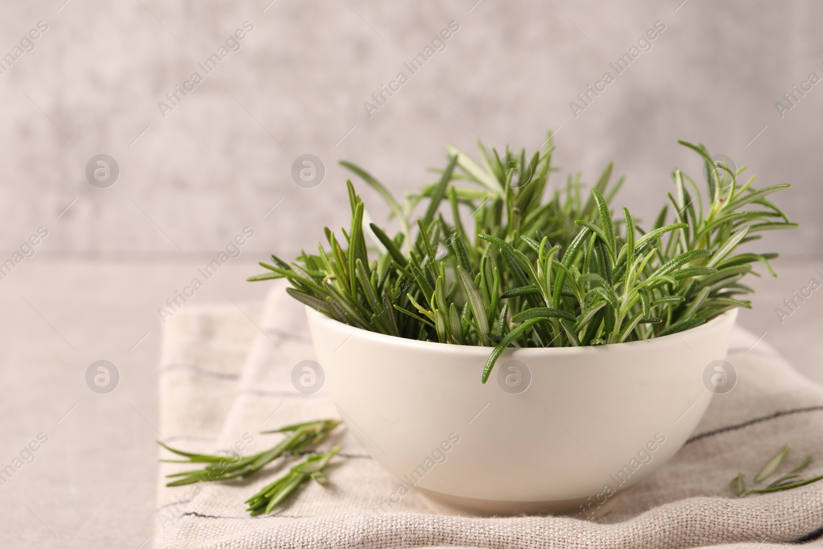 Photo of Bowl with fresh green rosemary on light grey table, closeup. Space for text