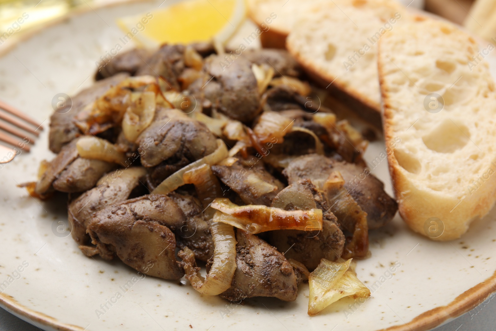 Photo of Tasty fried chicken liver with onion and bread on white table, closeup
