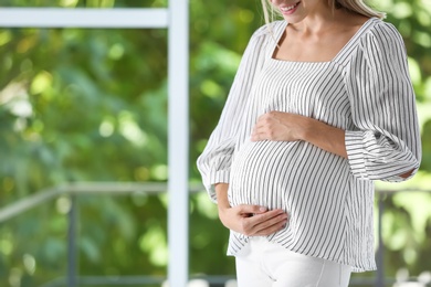 Photo of Pregnant woman standing near window at home, closeup