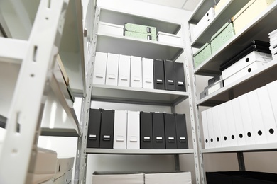 Photo of Folders and boxes with documents on shelves in archive, low angle view