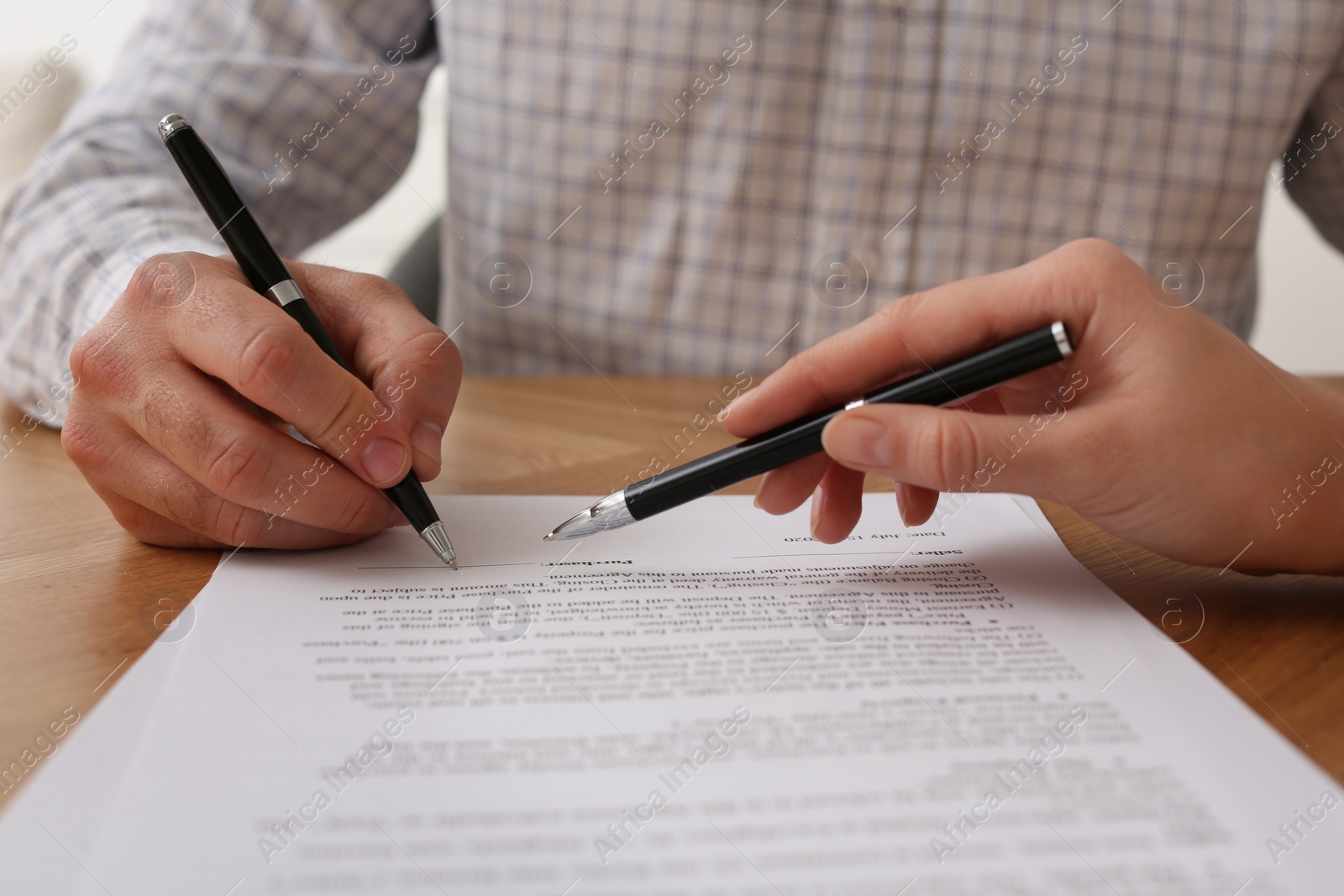 Photo of Businesspeople signing contract at wooden table, closeup of hands