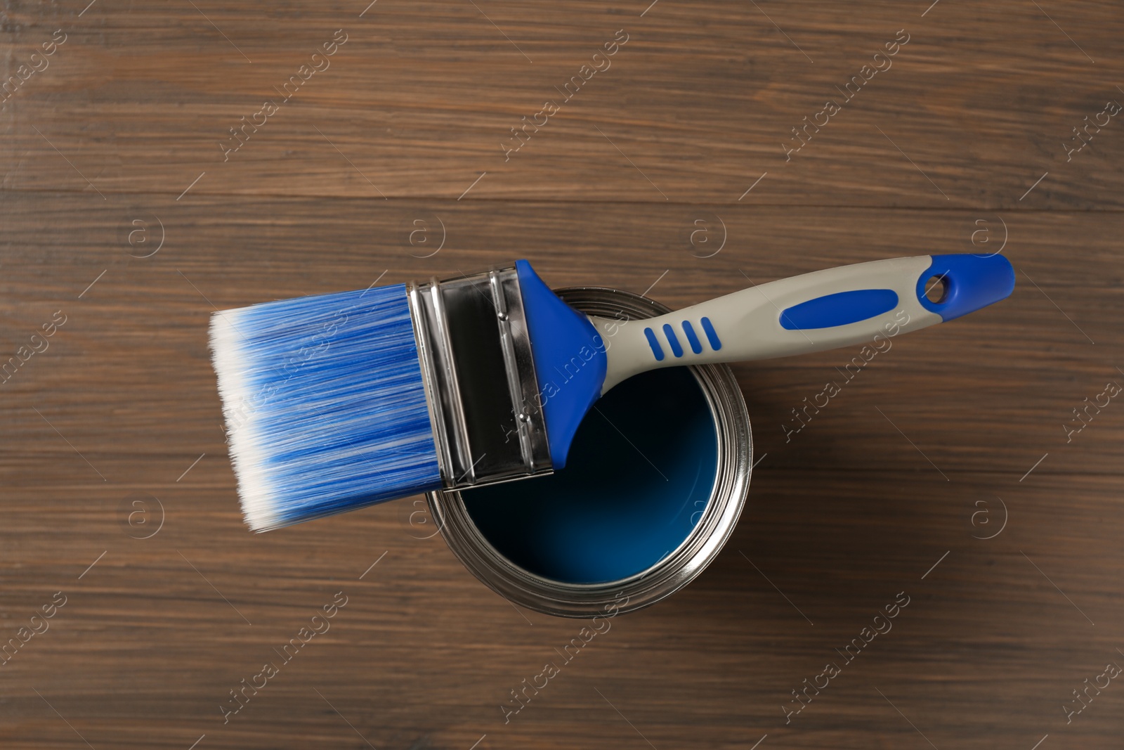 Photo of Can of blue paint and brush on wooden background, top view