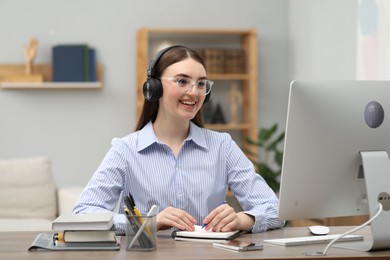 E-learning. Young woman taking notes during online lesson at table indoors