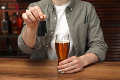 Photo of Man with glass of alcoholic drink holding car key at table in bar, closeup. Don't drink and drive concept