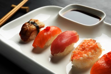 Plate with delicious nigiri sushi and soy sauce on black table, closeup