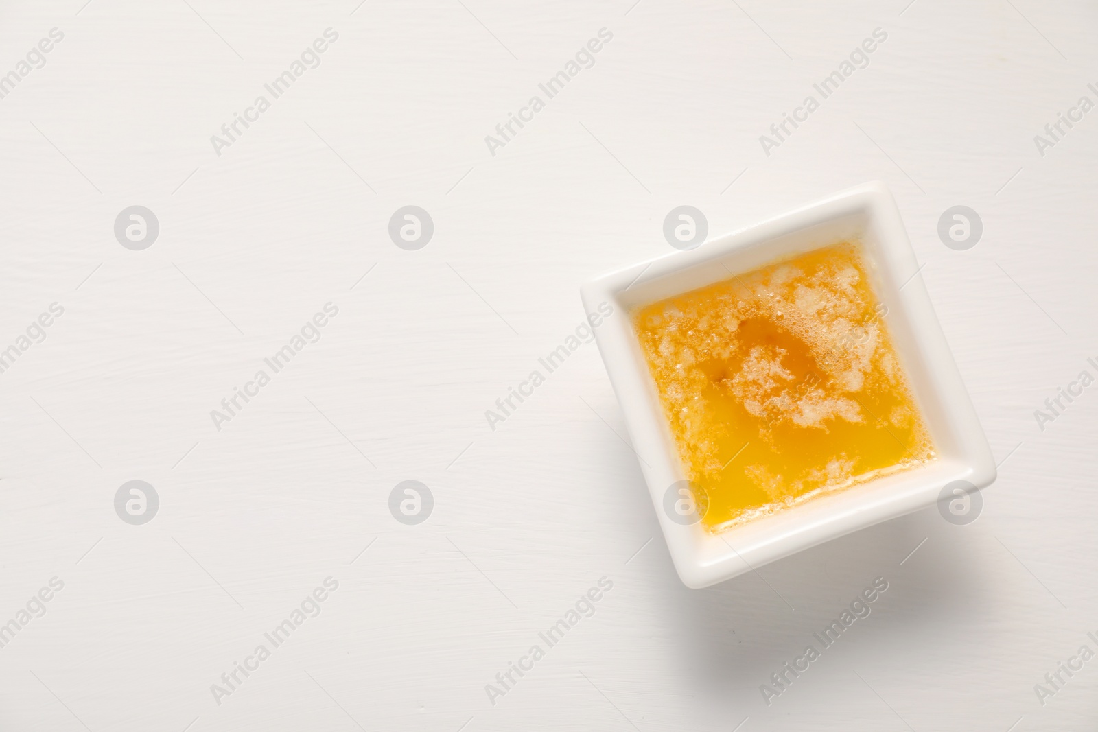 Photo of Melted butter in bowl on white wooden table, top view. Space for text