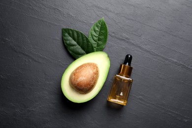 Photo of Bottle of essential oil, green leaves and fresh avocado on black table, flat lay