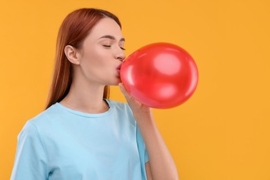 Woman inflating red balloon on orange background