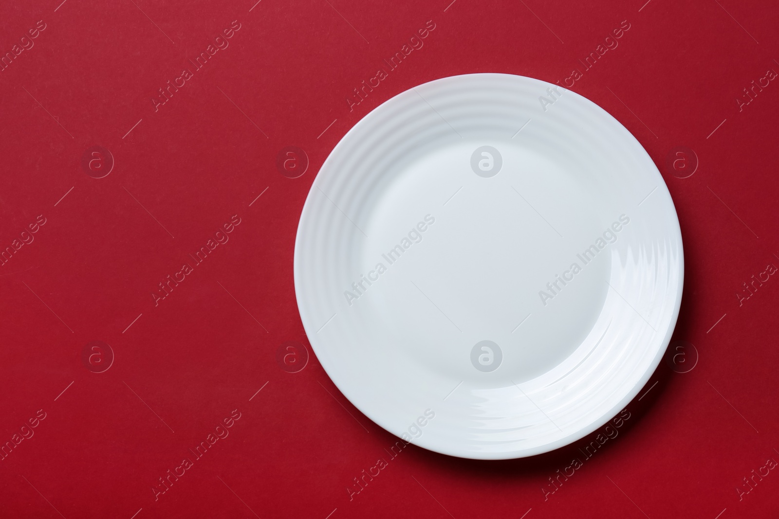 Photo of Empty white ceramic plate on red background, top view. Space for text