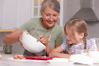 Happy grandmother with her granddaughter cooking together in kitchen