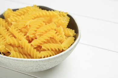 Photo of Raw fusilli pasta in bowl on white wooden table, closeup. Space for text