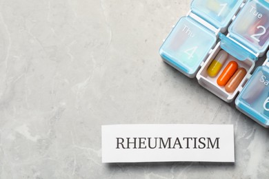 Card with word Rheumatism and pills on light gray marble table, flat lay. Space for text