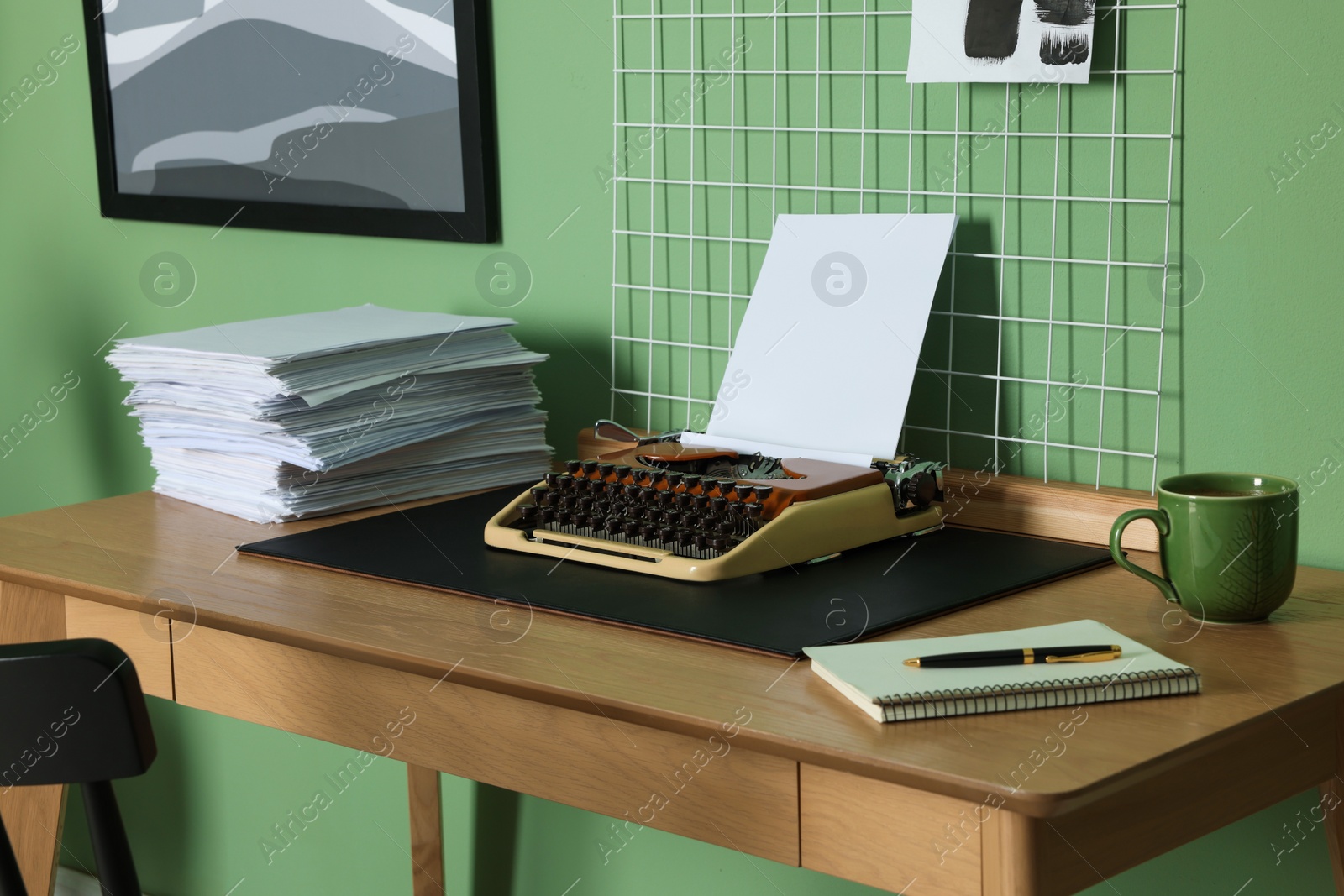 Photo of Typewriter, stack of papers and mood board on wooden table near pale green wall. Writer's workplace