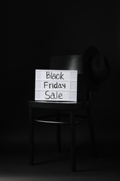 Photo of Chair, hat and board with phrase Black Friday Sale on dark background