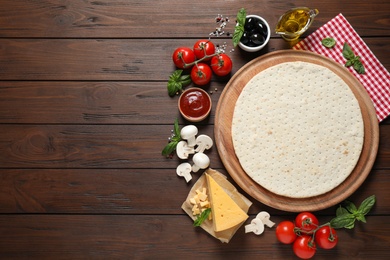 Flat lay composition with pizza crust and fresh ingredients on wooden table. Space for text