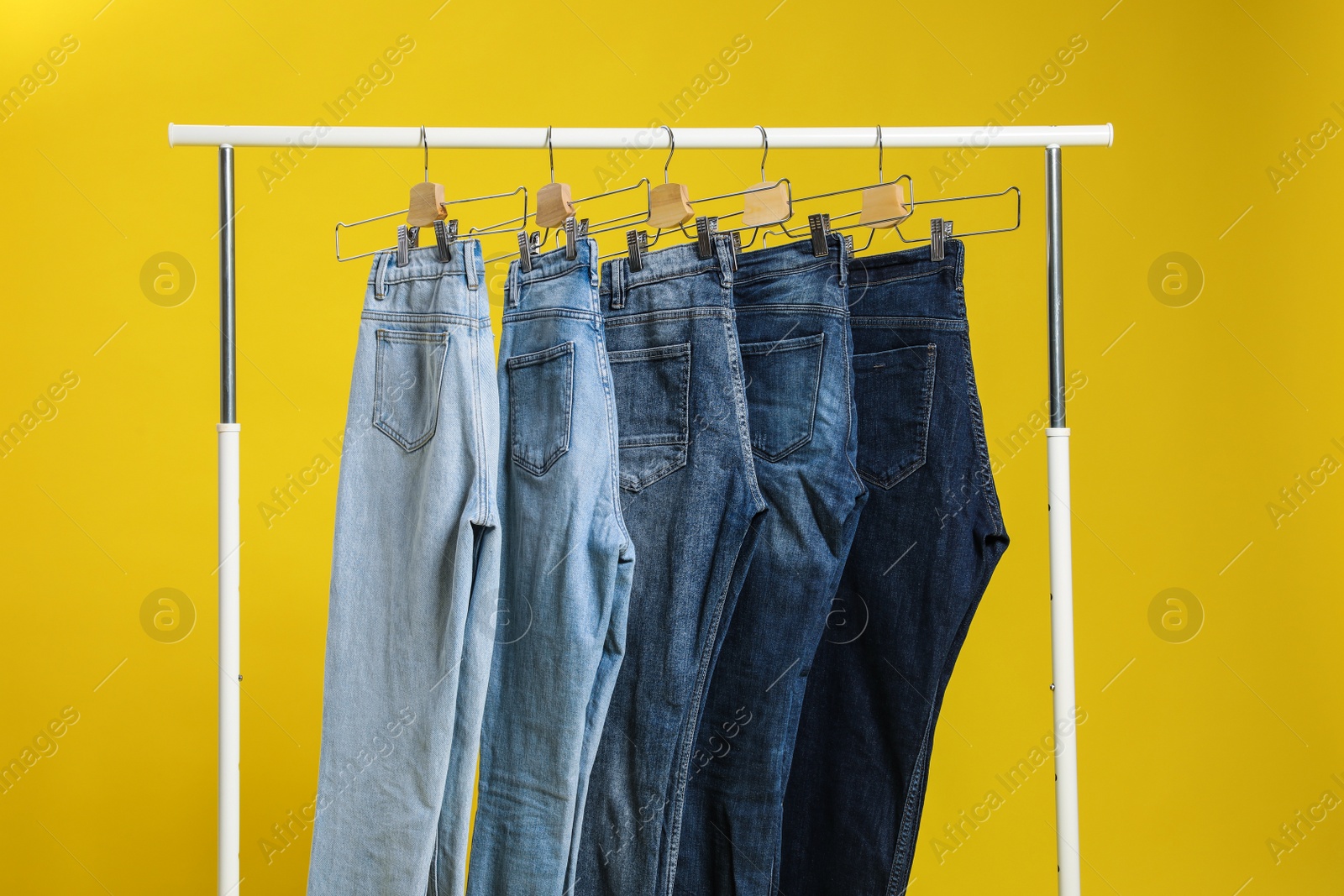 Photo of Rack with different jeans on yellow background