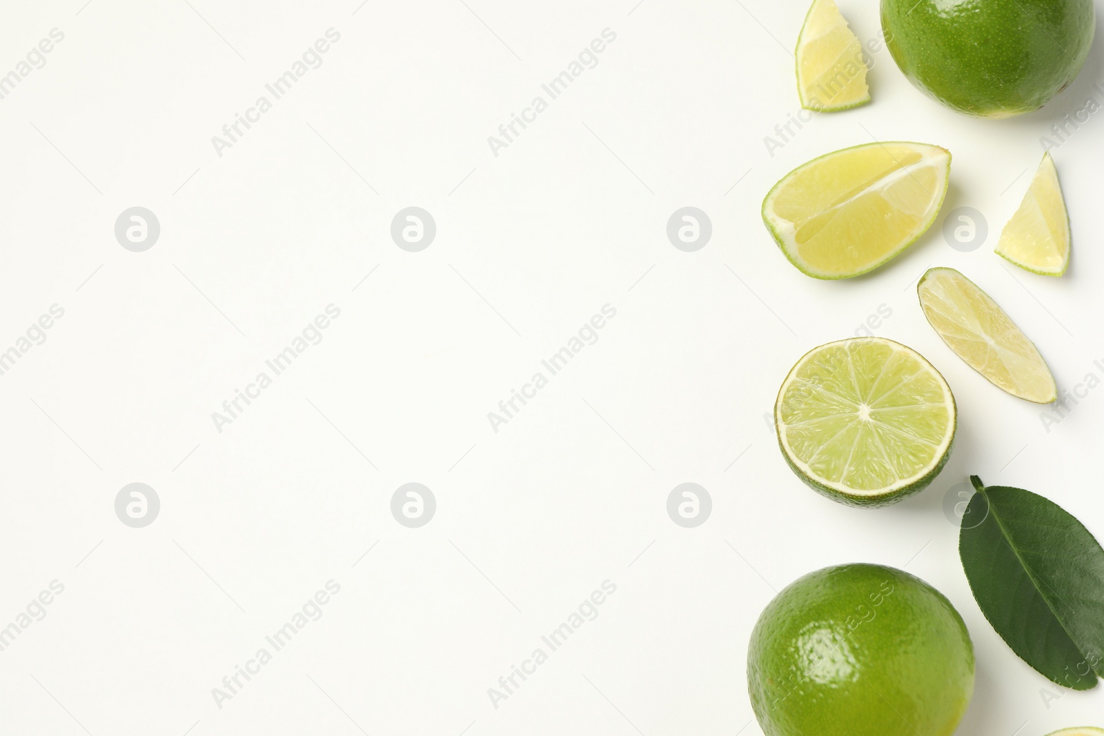 Photo of Whole and cut fresh ripe limes with green leaves on white background, flat lay