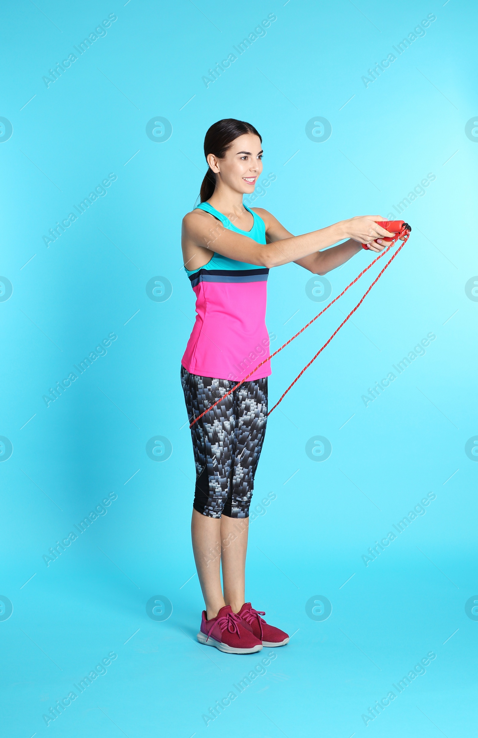 Photo of Full length portrait of young sportive woman training with jump rope on color background