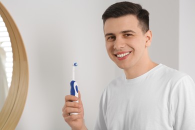 Happy man with electric toothbrush in bathroom