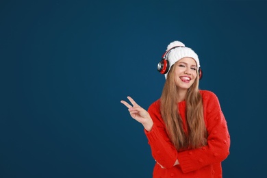 Young woman listening to music with headphones on dark blue background, space for text