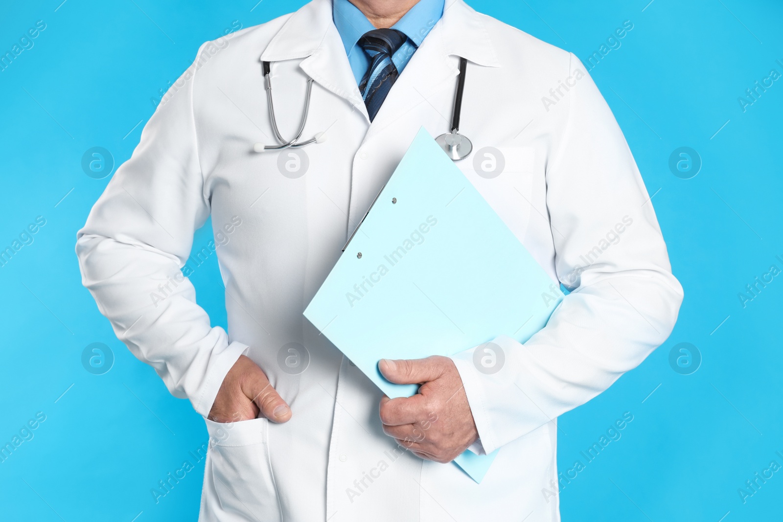 Photo of Senior doctor with clipboard on light blue background, closeup