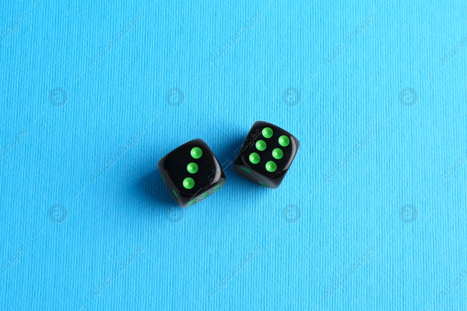 Photo of Two black game dices on light blue background, flat lay